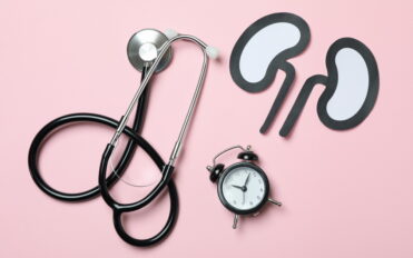 Alarm clock, paper kidneys and stethoscope on pink background